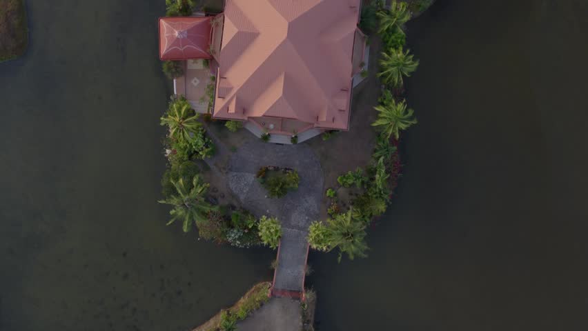 Top down aerial of a tropical mansion secluded house on a small island within freshwater fish ponds at sunset, drone