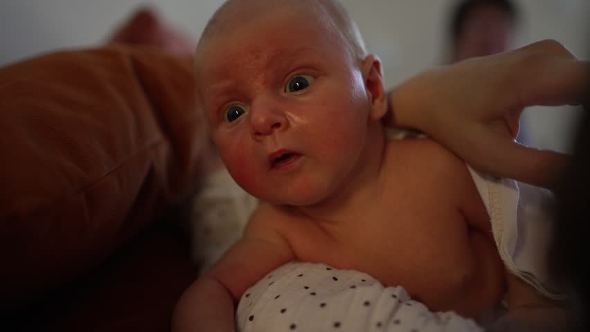 Adorable newborn baby with red cheeks and big curious eyes lying on his mother