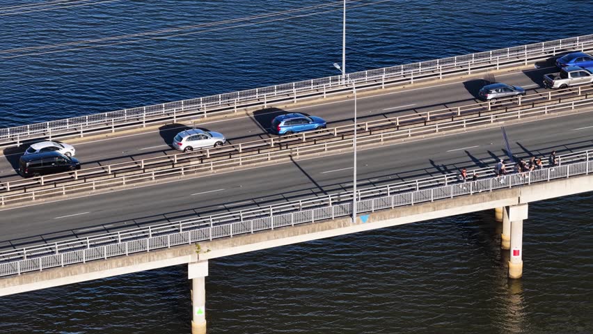 High-angle aerial shot of cars driving across a modern bridge over a blue river.