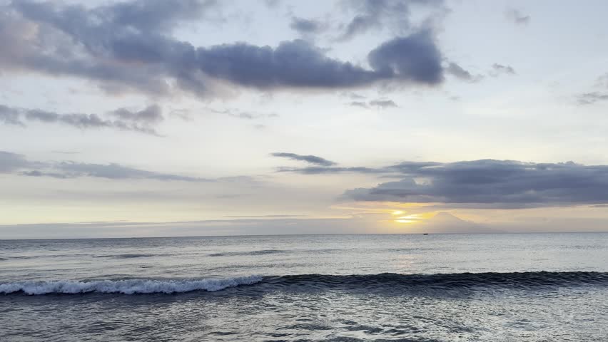 Serene sunset over the ocean with gentle waves and dramatic cloudy sky. A peaceful coastal scene capturing the golden hour as the sun sets on the horizon.