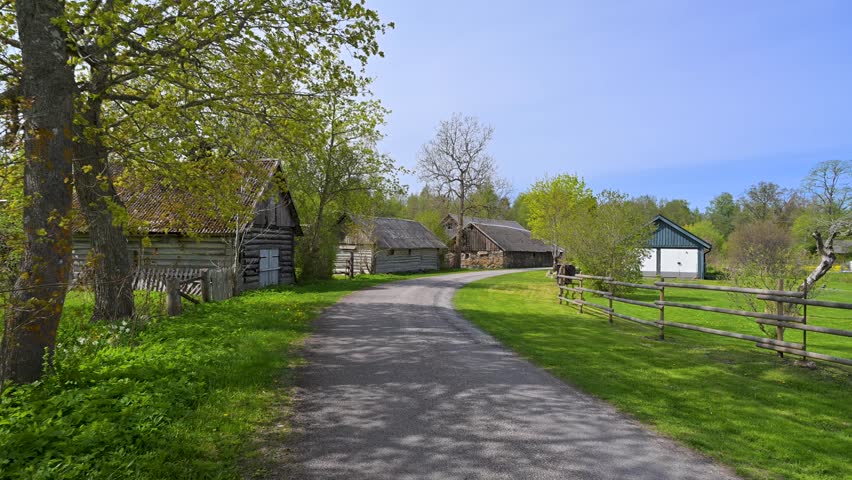 Sunny spring day view while walking down a country road in a traditional Estonian village with old wooden houses and lush green meadows