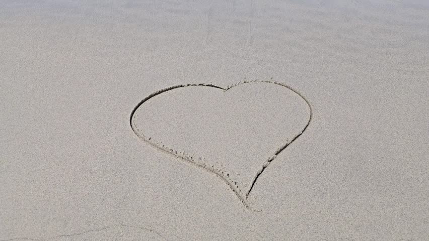 Sea wave washing away heart shape drawn in wet beach sand along shoreline. Love fading, broken relationship, impermanence, memories, romance and changing emotions concept.