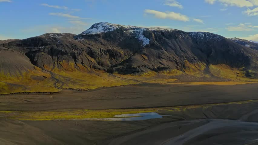 Aerial view of a majestic volcanic mountain valley with snow peak under a blue sky