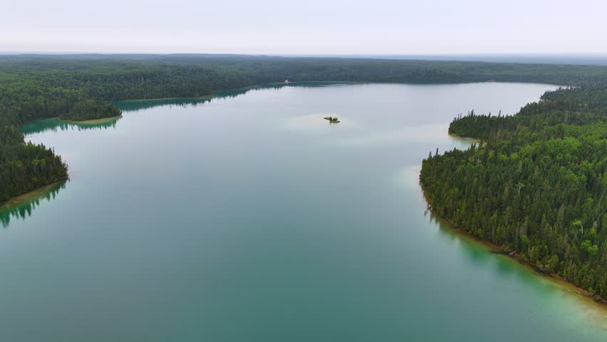 Aerial view of calm turquoise water reflecting an overcast sky, surrounded by dense boreal forest at Big Skunk Lake in Northern Ontario.