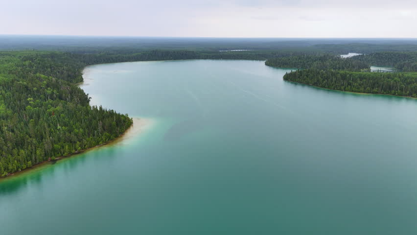 Aerial view of a turquoise lake surrounded by dense boreal forest in Northern Ontario. Big Skunk Lake stretches toward the horizon in a remote natural landscape.
