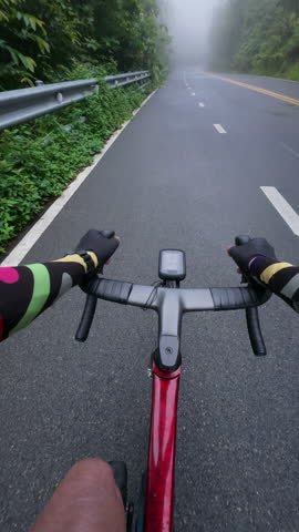 First-person point of view of a road cyclist riding along a foggy mountain road after rainfall through lush tropical forest. The immersive footage captures misty weather, wet pavement, scenic landscape, endurance cycling, outdoor adventure, and safe riding in low-visibility conditions.