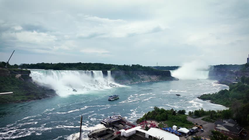 Tour boat approaches the American Falls as powerful water crashes over the cliffs, creating mist and dramatic scenery at Niagara Falls, Ontario, Canada.