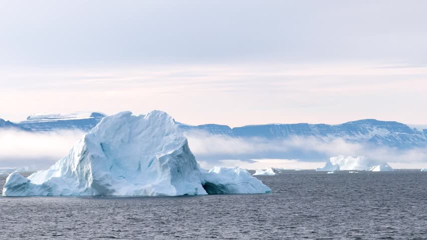 In Antarctica, icebergs float in the water while mountains rise in the background. The sun shines brightly on the snow and ice, creating a unique view of this remote area.