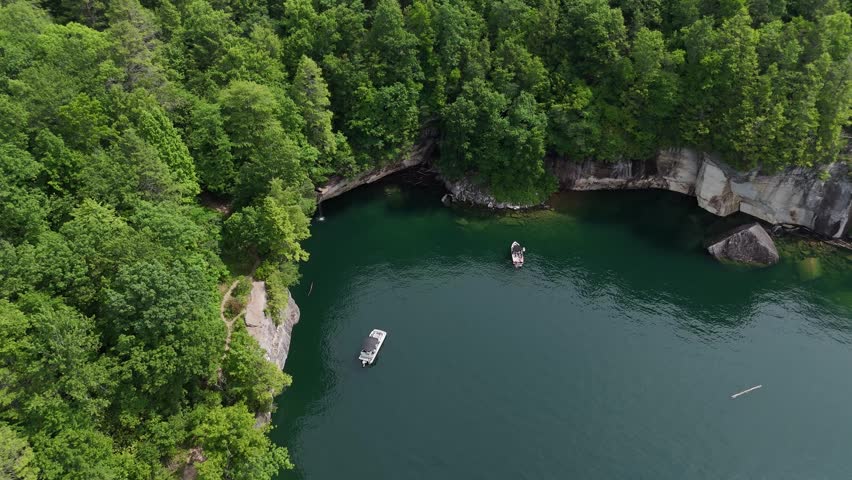 Aerial drone tracking shot over tiny boats cruising on the river surrounded by steep cliffs at New River Gorge National Park, West Virginia. Dense summer forest wilderness landscape.