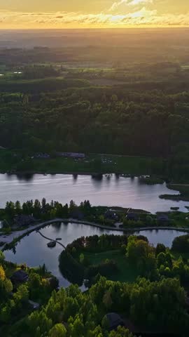 Aerial view of Amatciems village nestled among lush forests and serene lakes during a golden sunset in Amatciems, Cesu novads, Latvia.