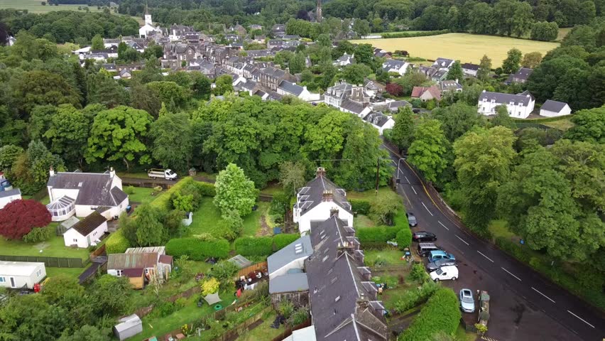 Peaceful aerial view of a small village nestled in lush greenery, with winding roads, quaint homes, and forested hills under a cloudy sky