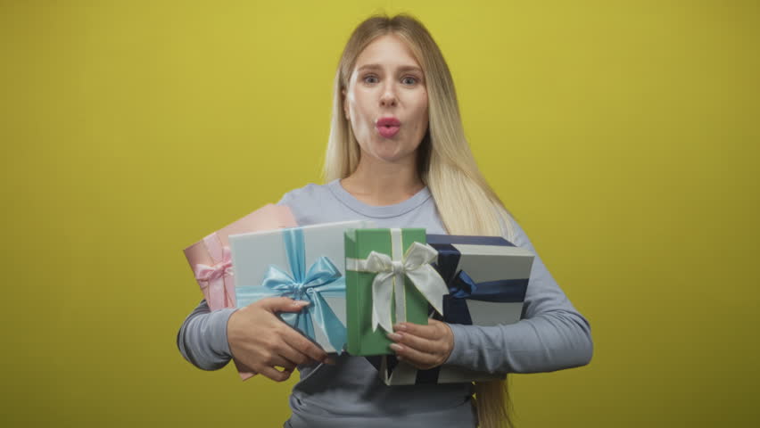 Woman holding multiple wrapped gift boxes with hands clasped, smiling and laughing in studio; celebration joy.