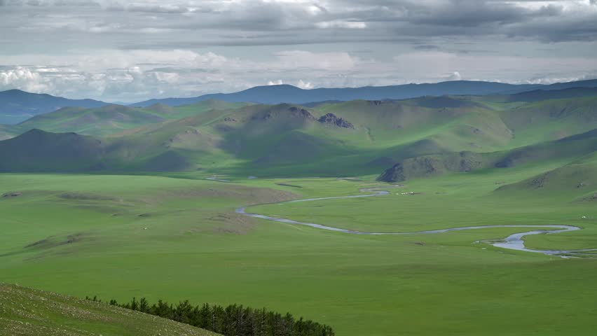 Panoramic Mongolian steppe shows rolling green hills rivers plus vast empty grasslands. Winding streams cross pristine plains with open countryside, natural serenity, remote quiet. Steppe rivers and small streams form green corridors that support meadow plants, wildlife, livestock, and seasonal camps. Meandering channels develop as flowing water erodes outer banks and deposits sediment along inner bends. The rolling relief and uninterrupted horizon show the large spatial scale of Mongolia