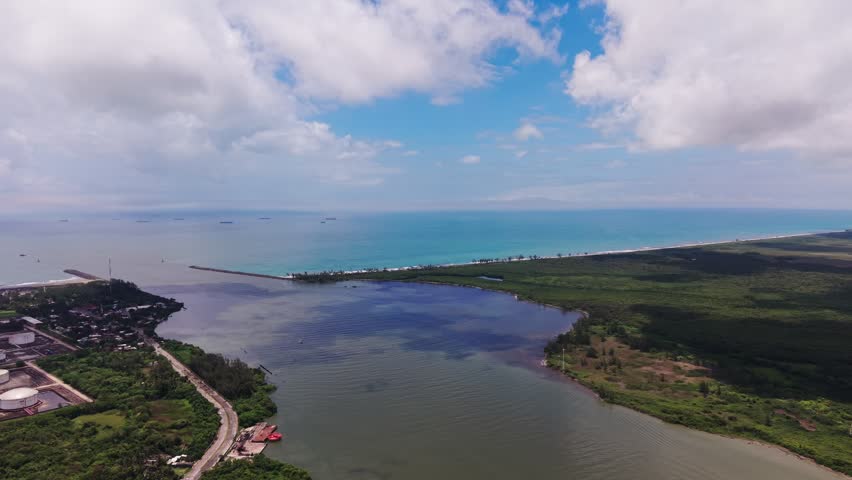 Aerial view of Tuxpan river mouth emptying into the Gulf of Mexico. Drone shot of industrial storage tanks, coastal road, and mangrove forest next to "La Mata" neigborhood in Veracruz, Mexico.