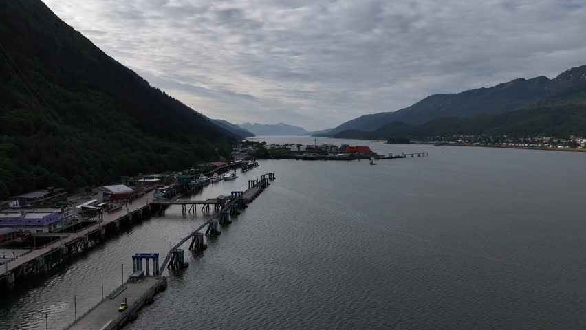 An aerial view of the port of Juneau situated between mountains, with a long pier extending into the calm water under cloudy sky in Alaska