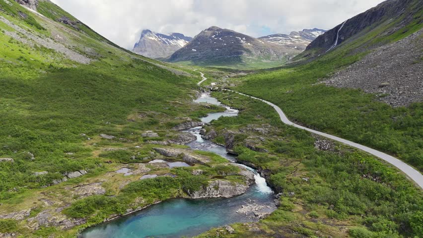 A drone view of a turquoise mountain river winding through Valldalen valley kayakers preparing to paddle near lush summer hills