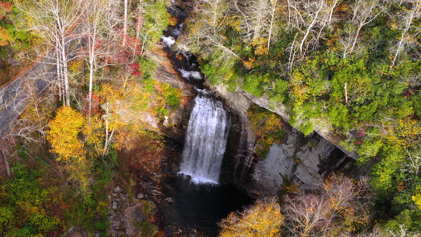 Autumn aerial view of Looking Glass Falls near Brevard, North Carolina. Visitors enjoy overlook as staircase leads toward the waterfall through vibrant forest.