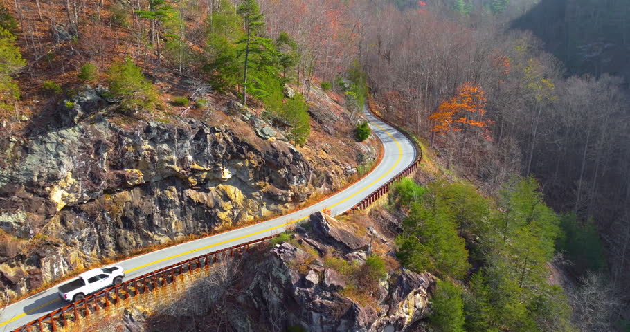 Car driving along Highlands Road, a scenic mountain pass in North Carolina. Steep rocky hillsides and vibrant fall foliage line the route