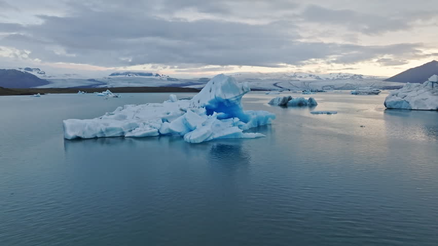 Cinematic aerial flight above floating blue icebergs in Jökulsárlón Glacier Lagoon, Iceland, revealing the breathtaking beauty of Vatnajökull glacier and the Arctic landscape at sunset.