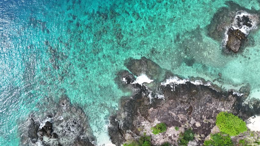 Clear turquoise ocean water washing over jagged volcanic rocks at the shore.