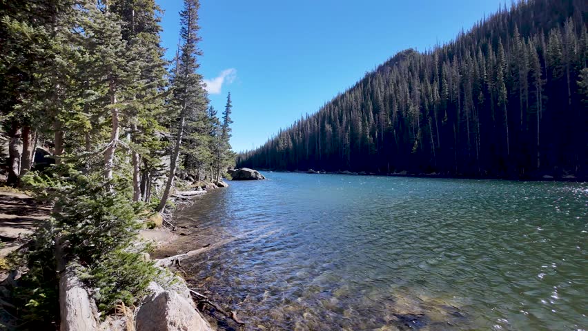 A slow pan across Dream Lake in Rocky Mountain National Park reveals sparkling water, evergreen forests, and mountain slopes along the scenic hiking trail.