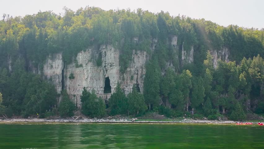 Cruising past Eagle Cave and the Niagara Escarpment reveals forested bluffs, distant kayakers, and Eagle Tower rising above Peninsula State Park in Door County.