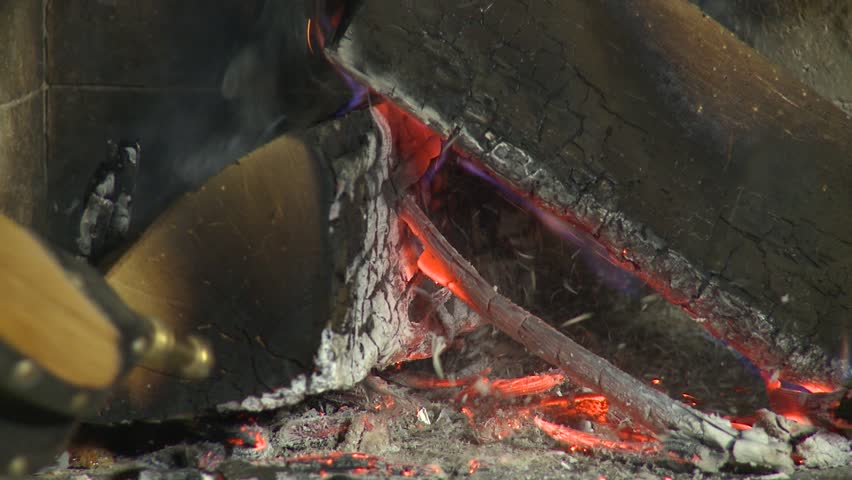 Close-up of fireplace bellows stoking flames, sparks and glowing embers around burning firewood in a cozy home hearth.