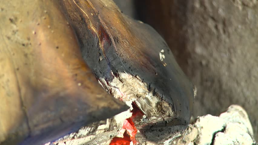 Static close-up of charred firewood, ash and glowing embers inside a fireplace, creating a warm rustic home heating atmosphere.