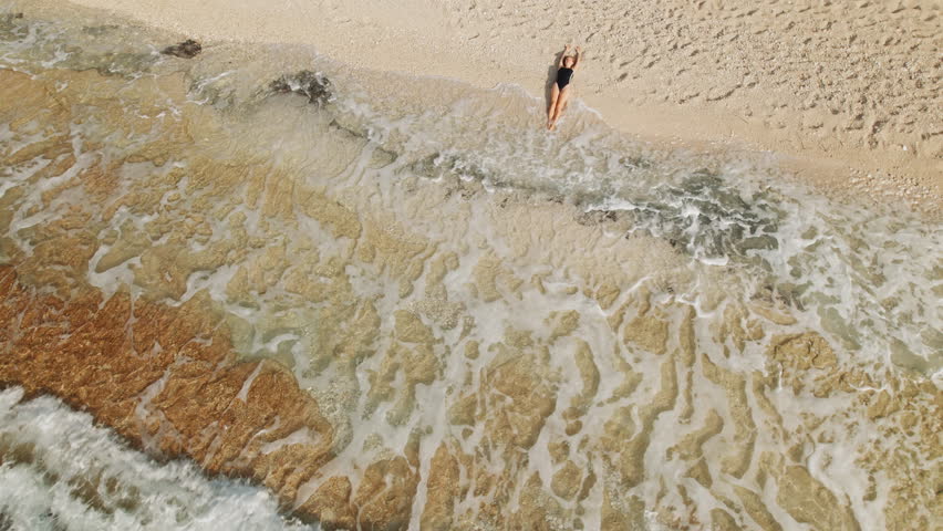 Woman relaxing on sandy beach near edge of gentle sea waves