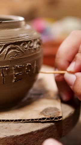 Close-up shot of hands using a tool to carve detailed designs into wet clay.