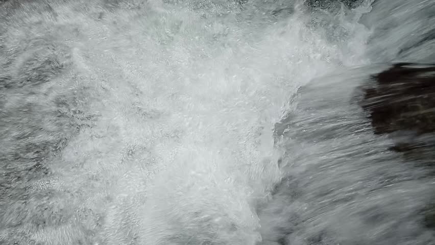 Top down view of rushing white foam and turbulent water downstream in a forest creek