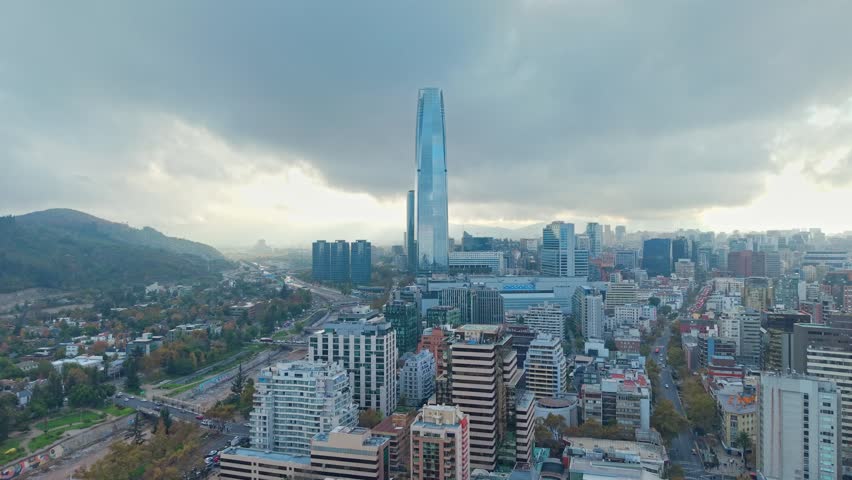 Aerial view dolly in of the Providencia neighborhood with the tall Costanera Tower, a modern building in Santiago, Chile, on a morning with a large gray cloud