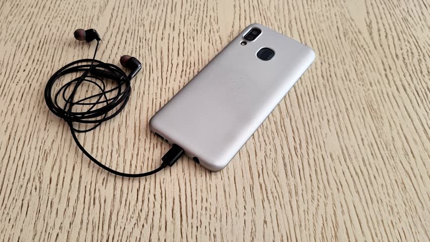 Disconnecting wired earphones from a smartphone after music and audio playback, showing everyday mobile technology, headphone use, and device connectivity