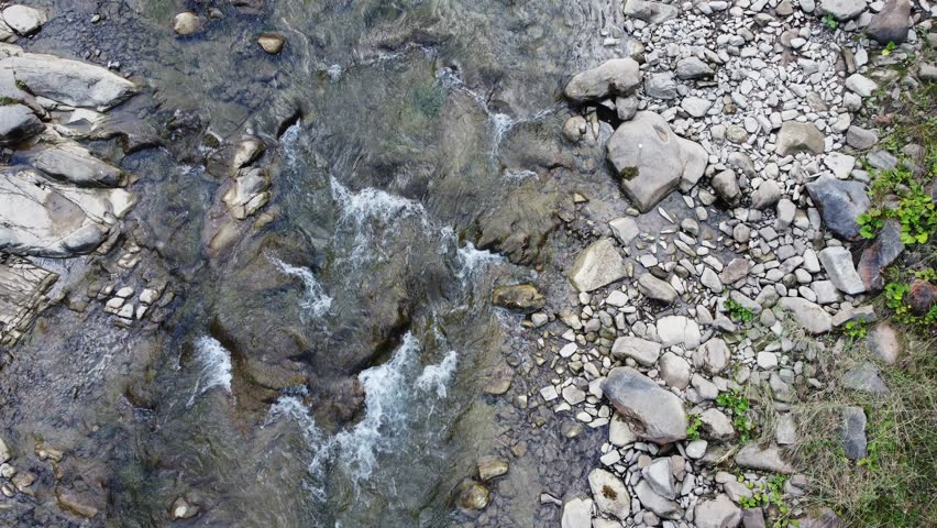 Water flow among the stones in a small mountain river in overcast day, aerial view vertically down while moving forward against the current
