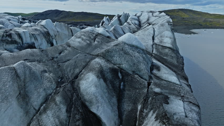 Cinematic aerial flight above the spectacular glacier front of Fjallsárlón Glacier Lagoon in Iceland, revealing deep crevasses, blue glacial ice and the dramatic landscape of Vatnajökull.