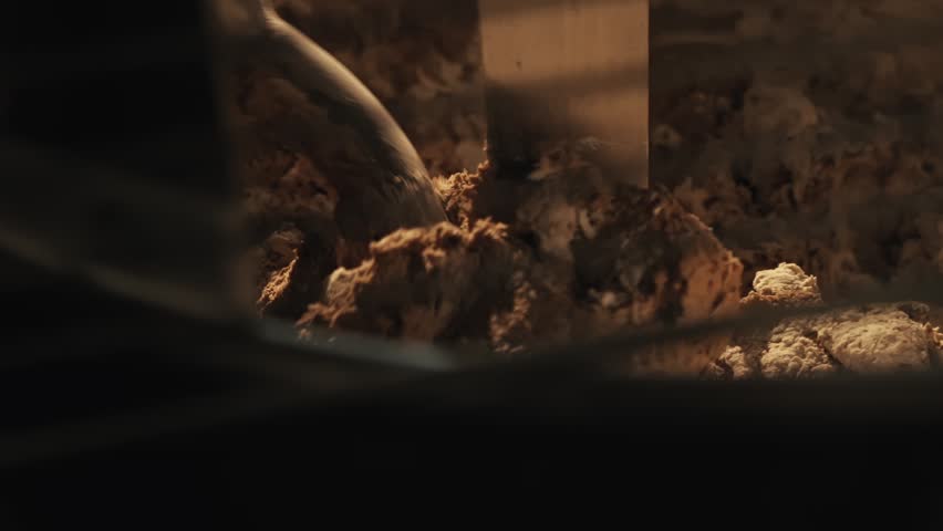 Close up, dough being kneaded by metal arm inside industrial spiral mixer during bread making process. Private bakery kitchen. Warm lighting