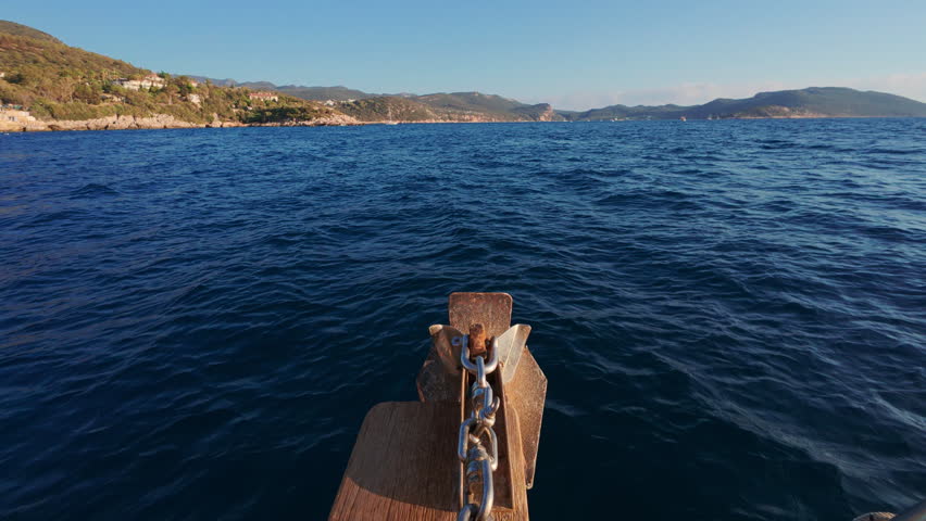 View from a boat sailing on a calm sea near a coastal area with hills and mountains in the distance during sunset or sunrise
