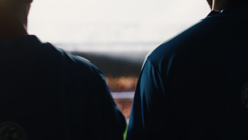 Footballers team waving to fans and walking onto pitch before game, raising hands toward packed stadium crowd in background blur, with team entrance moment on match day.