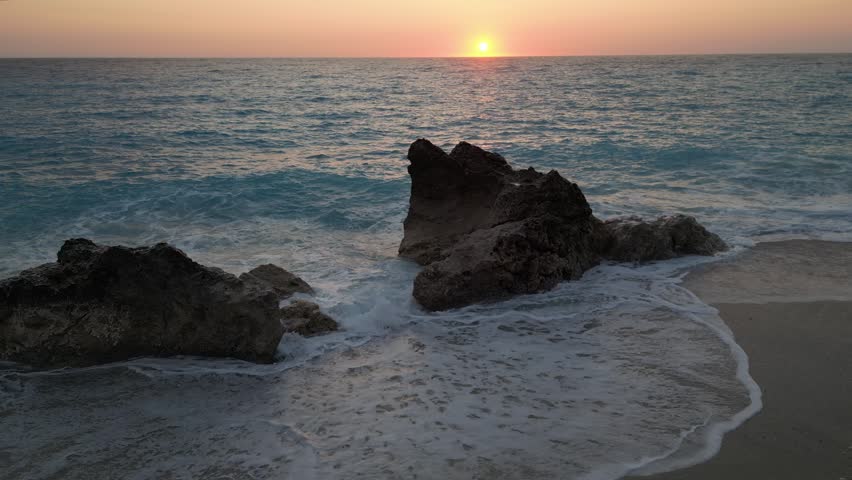 Calm ocean waves washing over rocks on a sandy beach during a beautiful and serene sunset