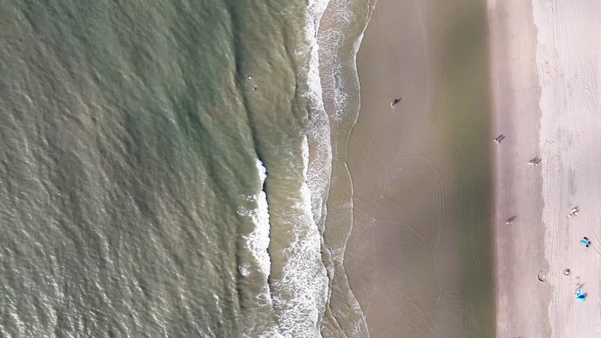 A top down aerial footage of the North Sea waves rolling on the sandy coast of Noordwijk city in the Netherlands on a sunny day