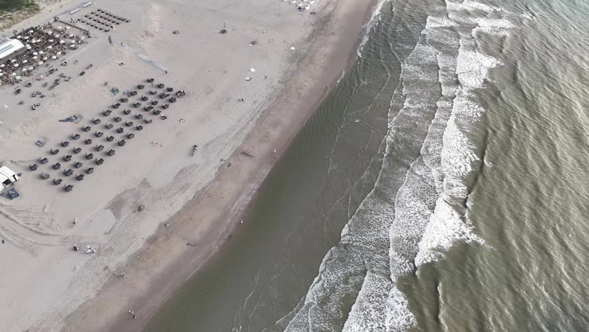 An aerial footage of the North Sea waves rolling on the sandy coast of Noordwijk city in the Netherlands on a sunny day