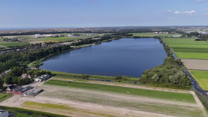 An aerial footage of the Oosterduinse Meer reservoir and swimming lake bordered by farmland and canal network in Noordwijkerhout, Netherlands