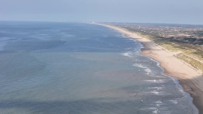 An aerial footage of the North Sea waves rolling along the sandy coast of Noordwijk city in the Netherlands during daytime