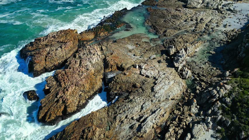 Cinematic drone view, rugged Atlantic coastline in Cape Town, South Africa, revealing rocky shoreline, crashing waves and dramatic coastal scenery from above