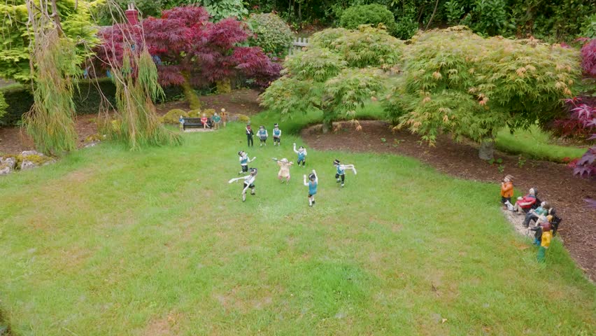 Miniature Morris dancers and musicians perform in Godshill model village, Isle of Wight. Camera pans left across a landscaped garden with tiny figures in traditional dress.