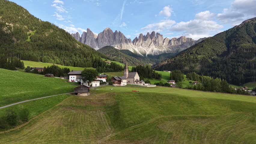 Aerial view of Santa Maddalena Church and alpine village among green meadows beneath the Odle Mountains in Val di Funes, Italy.
