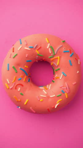 Rotating Glazed Donut with Sprinkles. Colorful donut turns smoothly on a pink background in a seamless loop.