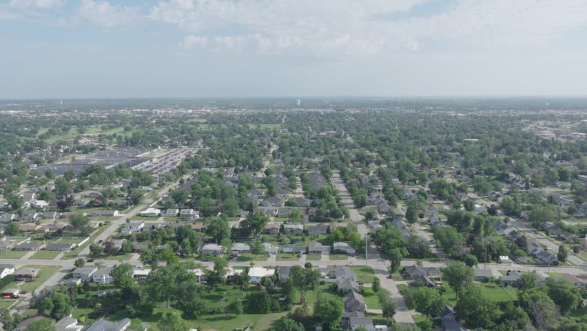 Aerial flyover glides over sprawling suburban homes in Cedar Rapids Iowa showing grid pattern streets, dense tree canopy and distant skyline