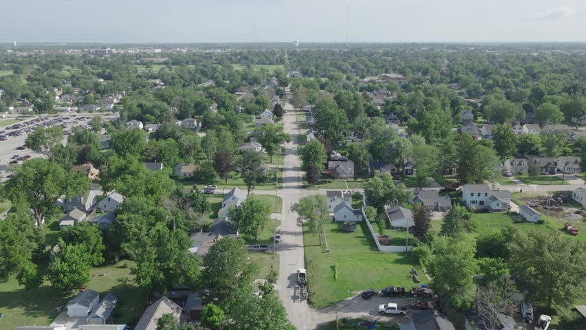 Drone flies over quiet residential neighborhood street lined with houses and trees in Cedar Rapids Iowa with water tower on horizon