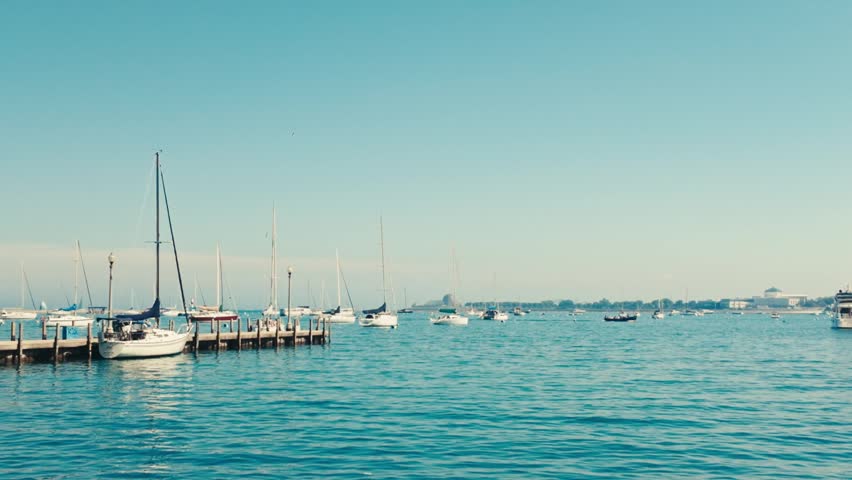A panning shot of sailboats in a harbor and on a dock on a summer day on Lake Michigan.